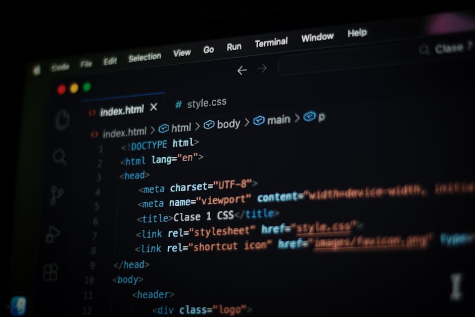 Close-up of a person's hands operating a laptop on a dark desk, displaying a code editor with lines of colourful programming code on the screen. The laptop is positioned on a black surface, and the ba